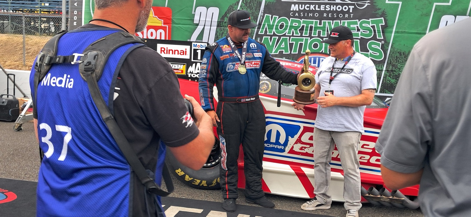 Funny Car driver Matt Hagan in his Direct Connection firesuit holding the winner trophy at the NHRA Northwest Nationals